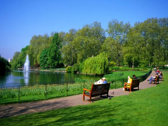 A peaceful pathway winding through the lush green trees and ornamental gardens of Hyde Park, London, on a sunny day.