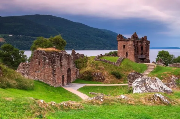 The calm, expansive waters of Loch Ness surrounded by the misty hills of the Scottish Highlands.
