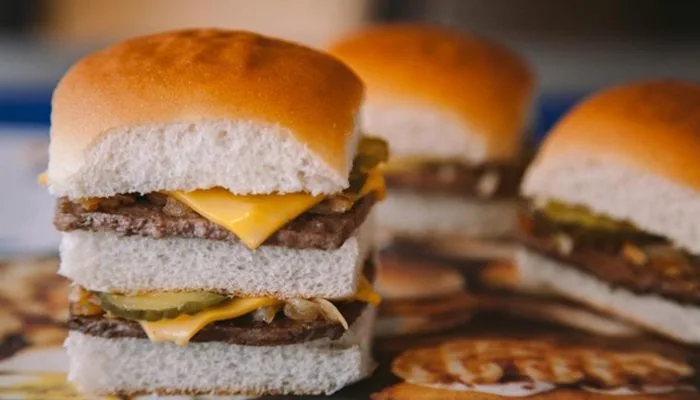 Classic American square sliders on a wooden board with onions and pickles